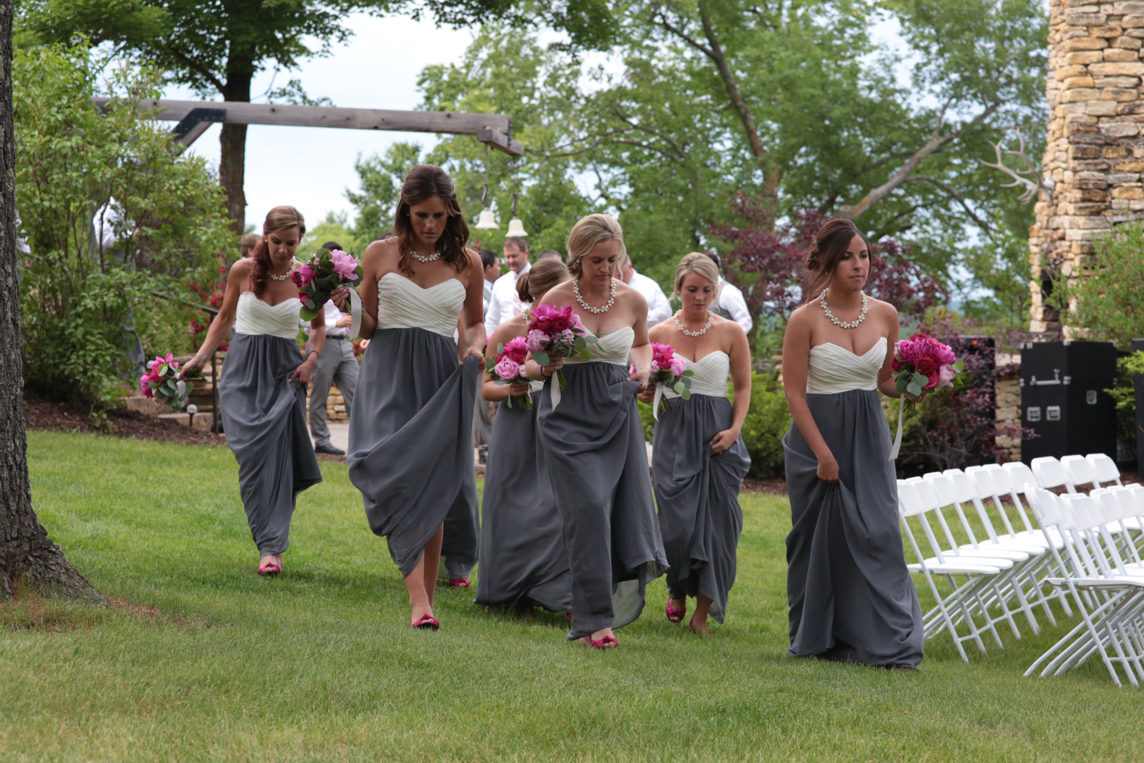 Bridesmaids walking toward ceremony site at BWB Ranch Party Venue in Laporte Minnesota, captured by photographer Amy Kate Photography. Bridesmaids with long grey dresses, white sleeveless sweet heart tops.